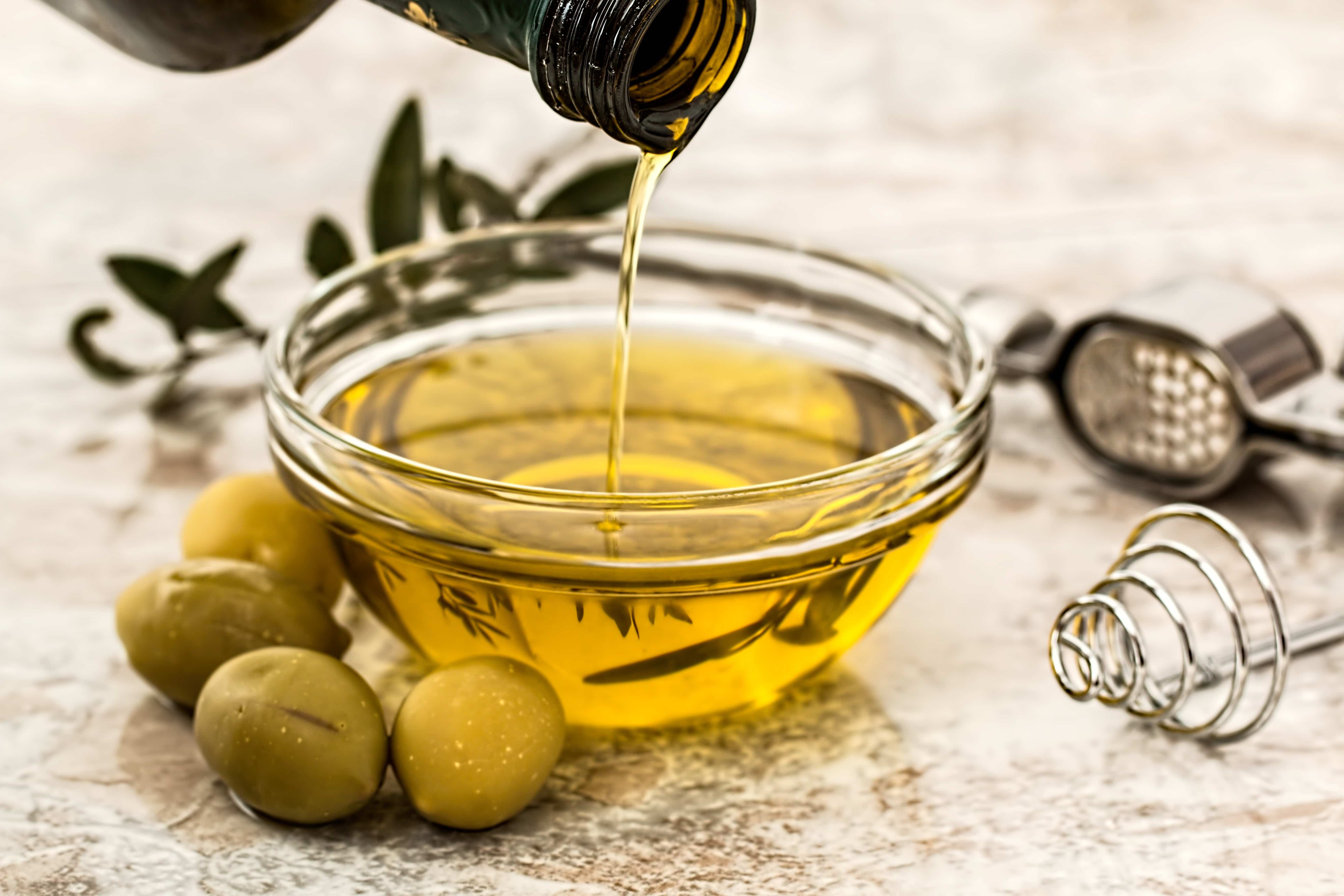 fles olijfolie in schaaltje en olijven ernaast